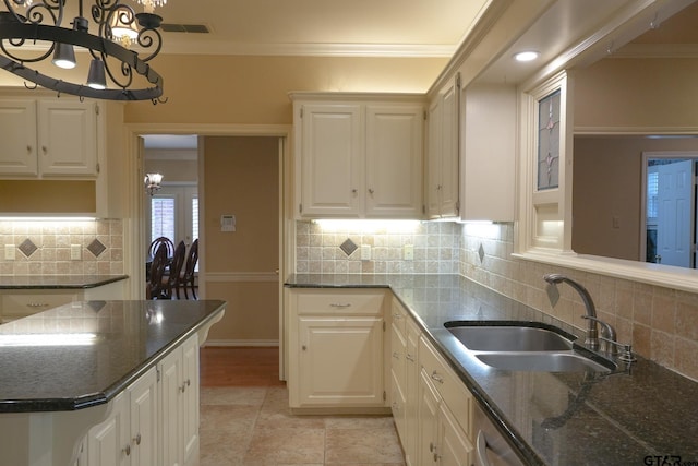 kitchen with sink, tasteful backsplash, ornamental molding, white cabinets, and dark stone counters