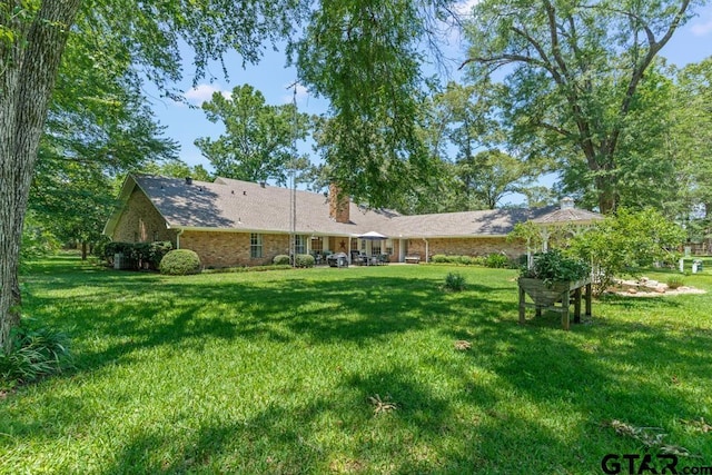 1805 Greenway St, Gilmer, TX 75644 - back of house featuring a chimney, a lawn, and brick siding