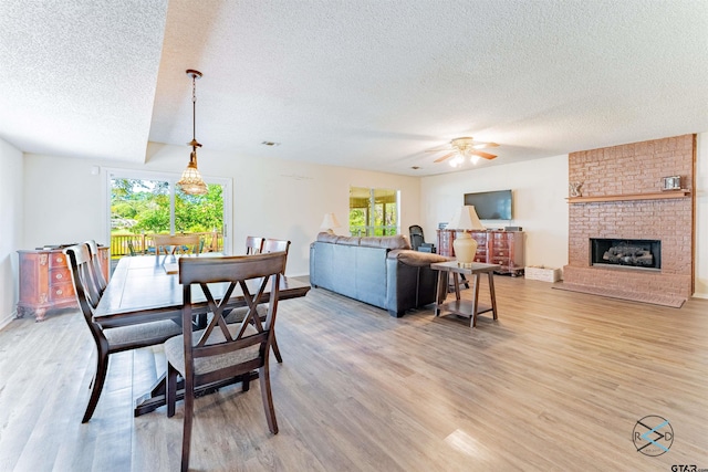 dining room featuring a fireplace, hardwood / wood-style flooring, ceiling fan, and a textured ceiling