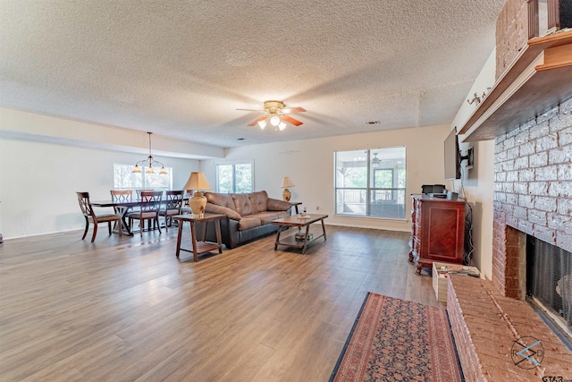 living room with a fireplace, hardwood / wood-style flooring, ceiling fan with notable chandelier, and a textured ceiling