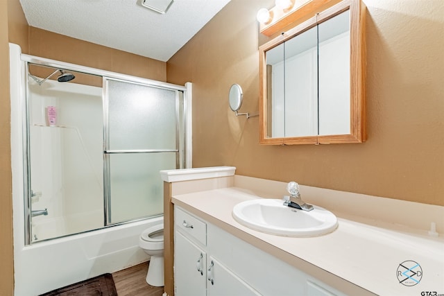 full bathroom featuring enclosed tub / shower combo, vanity, a textured ceiling, hardwood / wood-style flooring, and toilet