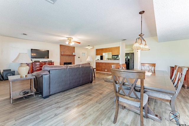 dining area with hardwood / wood-style floors, ceiling fan, a textured ceiling, and a brick fireplace