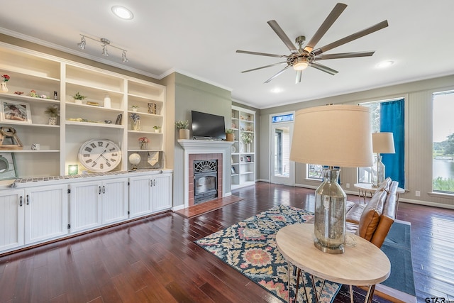 living room with crown molding, ceiling fan, built in features, a fireplace, and dark hardwood / wood-style flooring