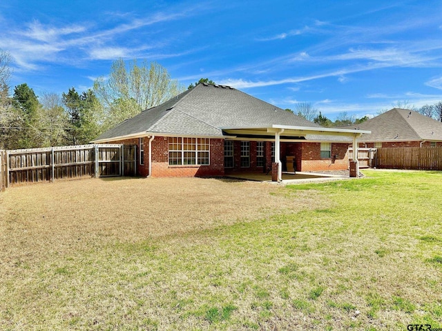 back of house with brick siding, a shingled roof, a fenced backyard, a yard, and a patio area