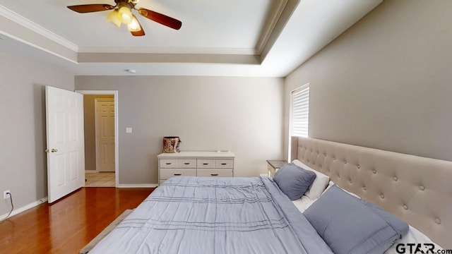 bedroom featuring ceiling fan, baseboards, ornamental molding, wood finished floors, and a raised ceiling