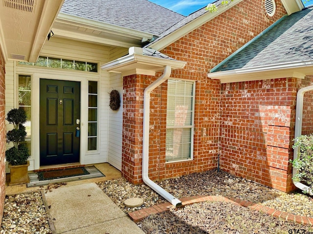 property entrance featuring brick siding and roof with shingles