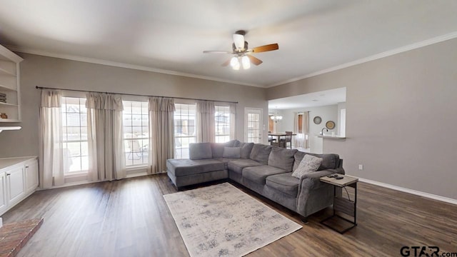 living area featuring dark wood-type flooring, crown molding, ceiling fan with notable chandelier, and baseboards