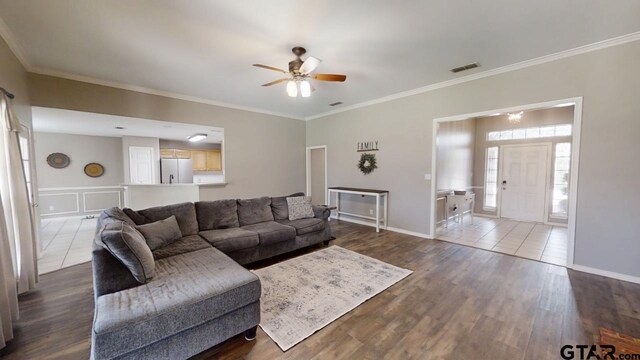 living room featuring dark wood-style floors, visible vents, ceiling fan, and ornamental molding