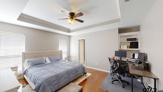 bedroom featuring a raised ceiling, wood finished floors, and baseboards