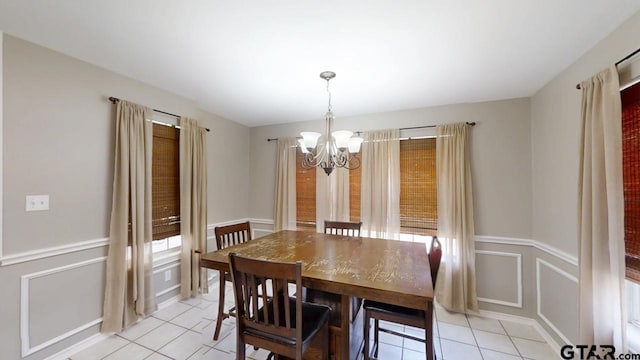 dining room with light tile patterned floors, a notable chandelier, a decorative wall, and a wainscoted wall