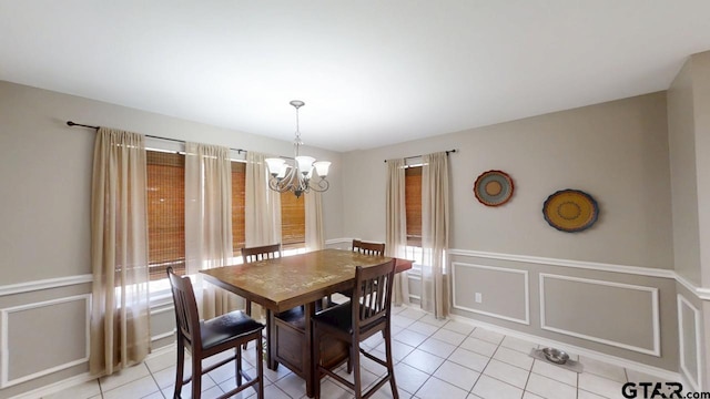 dining area featuring wainscoting, a chandelier, light tile patterned flooring, and a decorative wall