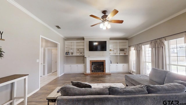 living room featuring visible vents, ornamental molding, a ceiling fan, wood finished floors, and a fireplace