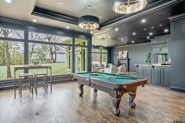 recreation room featuring a tray ceiling, recessed lighting, wood finished floors, and crown molding