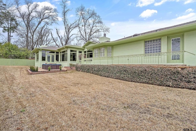 rear view of property featuring brick siding, fence, a sunroom, a chimney, and a hot tub