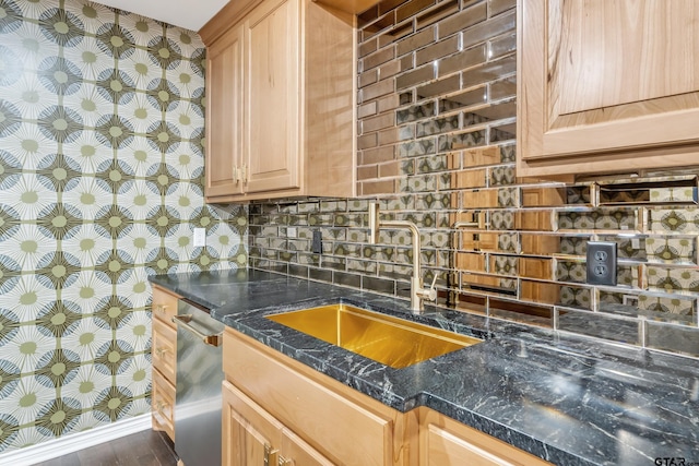 kitchen with backsplash, stainless steel dishwasher, a sink, baseboards, and wallpapered walls