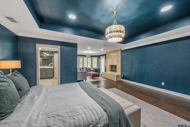 bedroom featuring baseboards, visible vents, wood finished floors, a tray ceiling, and a chandelier