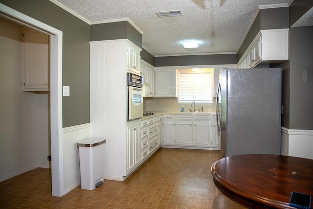 3505 Cloverdale Dr, Tyler, TX 75701 - kitchen with freestanding refrigerator, oven, a sink, white cabinets, and wainscoting