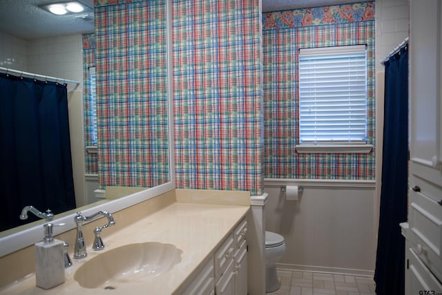 3505 Cloverdale Dr, Tyler, TX 75701 - bathroom with vanity, toilet, a wainscoted wall, a textured ceiling, and wallpapered walls