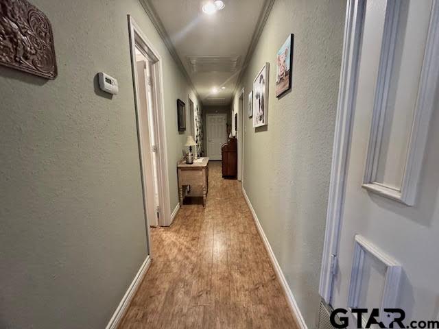 corridor featuring a textured wall, baseboards, and light wood finished floors