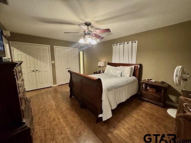 bedroom with a textured ceiling, two closets, ceiling fan, and dark hardwood / wood-style floors