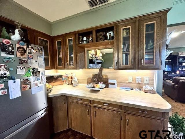 kitchen with visible vents, freestanding refrigerator, ornamental molding, light countertops, and glass insert cabinets