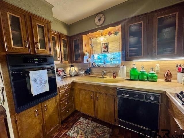 kitchen with black appliances, a sink, backsplash, light countertops, and glass insert cabinets