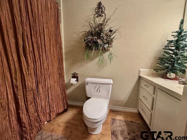 bathroom with toilet, vanity, baseboards, and a textured wall