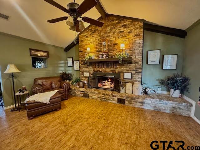 living room featuring hardwood / wood-style flooring, vaulted ceiling with beams, ceiling fan, and a brick fireplace