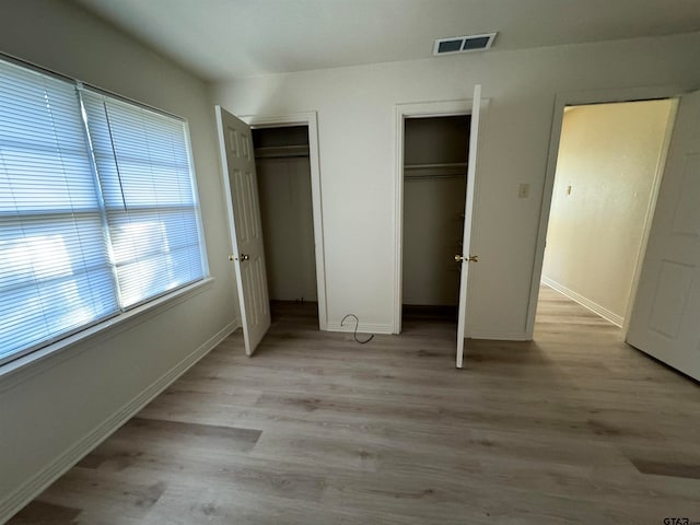 unfurnished bedroom with two closets and light wood-type flooring