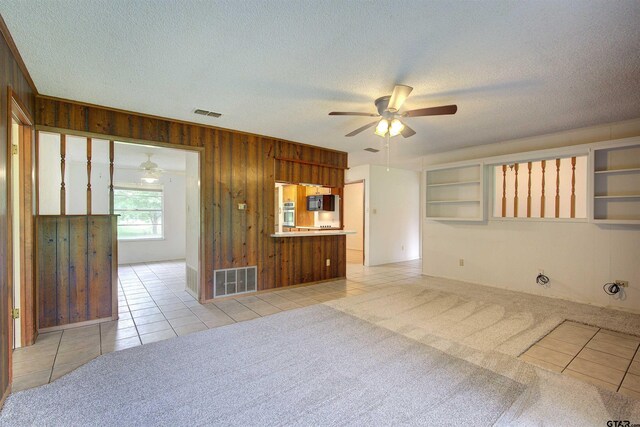 19870 Fm 1253, Lindale, TX 75771 - unfurnished living room with a ceiling fan, wood walls, light tile patterned floors, a textured ceiling, and light colored carpet