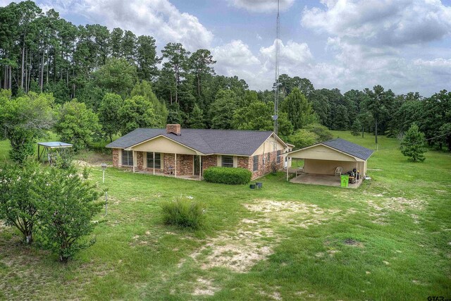 19870 Fm 1253, Lindale, TX 75771 - view of front of house featuring a front yard, a chimney, covered porch, a wooded view, and a detached carport