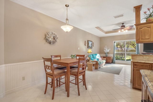 dining area with a textured ceiling, a tray ceiling, ceiling fan, and ornamental molding