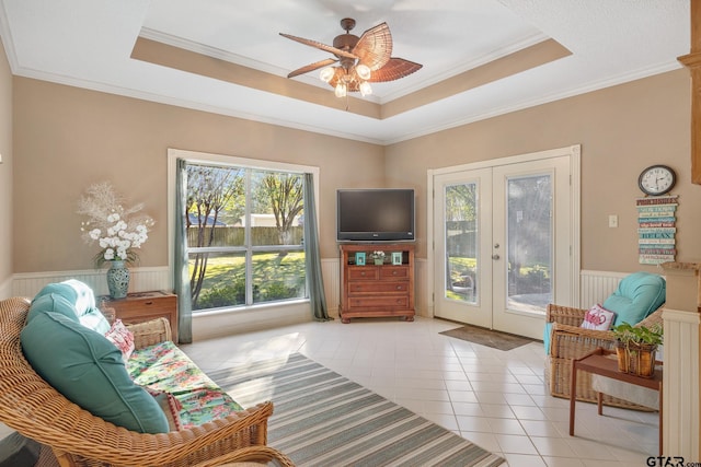 tiled living room with ceiling fan, a raised ceiling, crown molding, and french doors