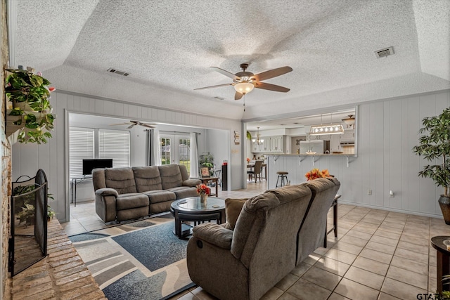 living area with a textured ceiling, light tile patterned floors, visible vents, and ceiling fan