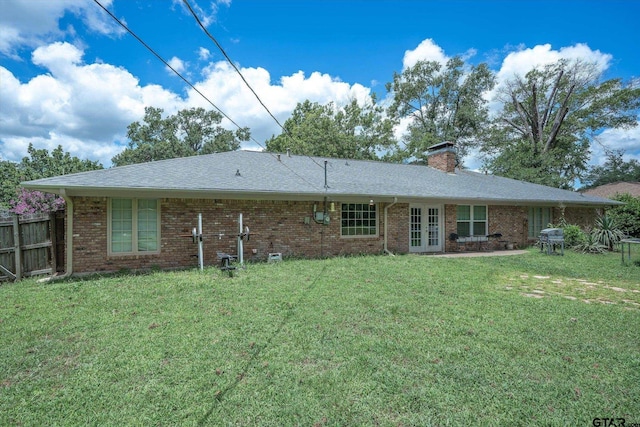 back of property with fence, a yard, a chimney, french doors, and brick siding