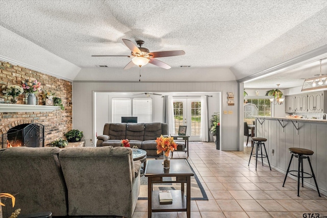 living area with light tile patterned floors, lofted ceiling, a fireplace, ceiling fan, and french doors