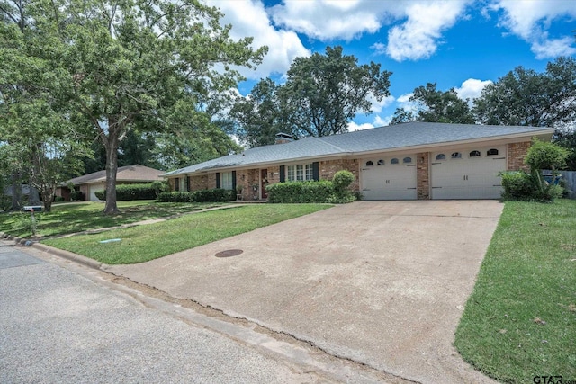 ranch-style home featuring a front yard, driveway, a chimney, a garage, and brick siding