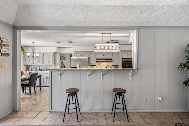 kitchen with a breakfast bar, hanging light fixtures, a textured ceiling, black oven, and stainless steel fridge