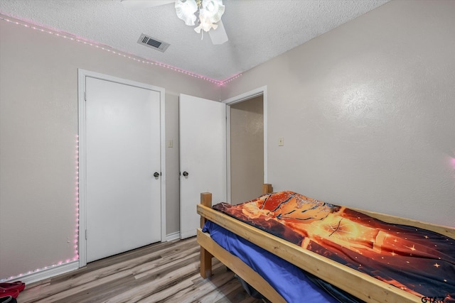 bedroom with a ceiling fan, wood finished floors, visible vents, and a textured ceiling