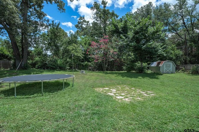 view of yard with a shed, an outdoor structure, a trampoline, and fence