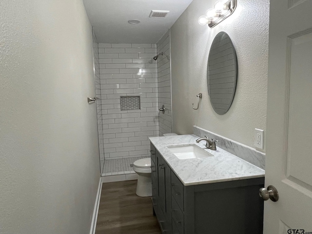 bathroom with toilet, wood-type flooring, a tile shower, and vanity