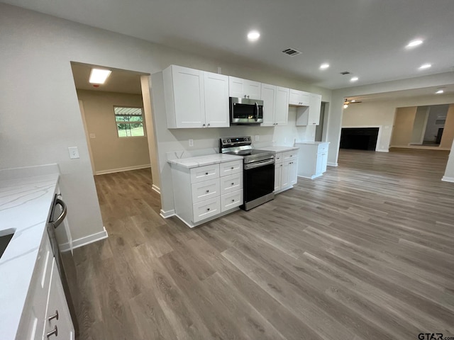 kitchen with white cabinets, light hardwood / wood-style floors, light stone countertops, and appliances with stainless steel finishes