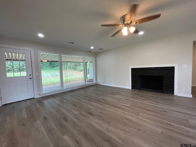 unfurnished living room featuring a brick fireplace, dark hardwood / wood-style floors, and ceiling fan