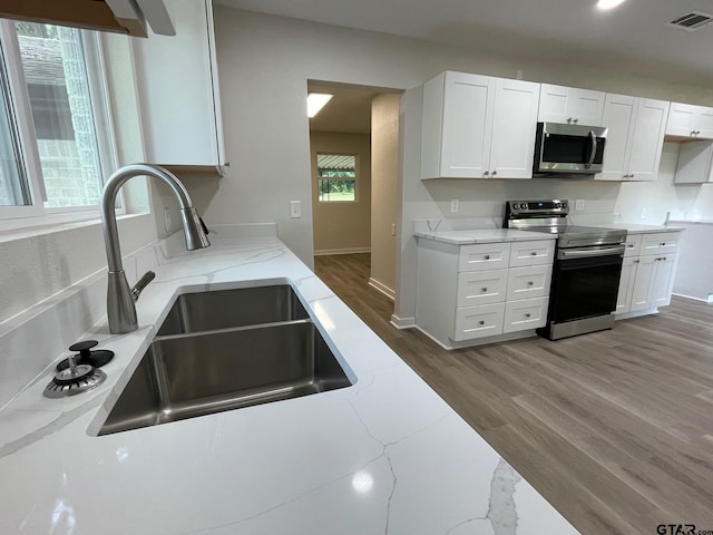 kitchen with light stone countertops, appliances with stainless steel finishes, sink, and white cabinets