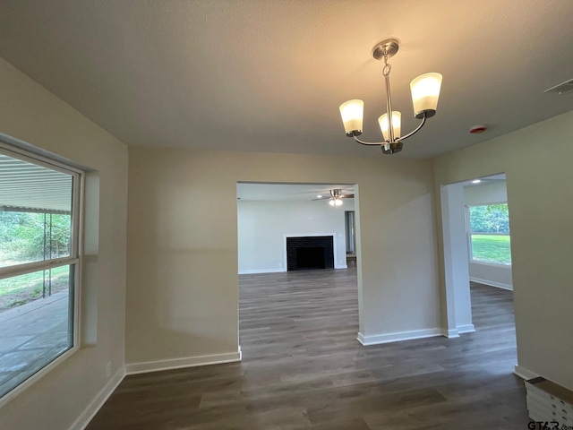 unfurnished dining area featuring a brick fireplace, ceiling fan with notable chandelier, and dark hardwood / wood-style flooring