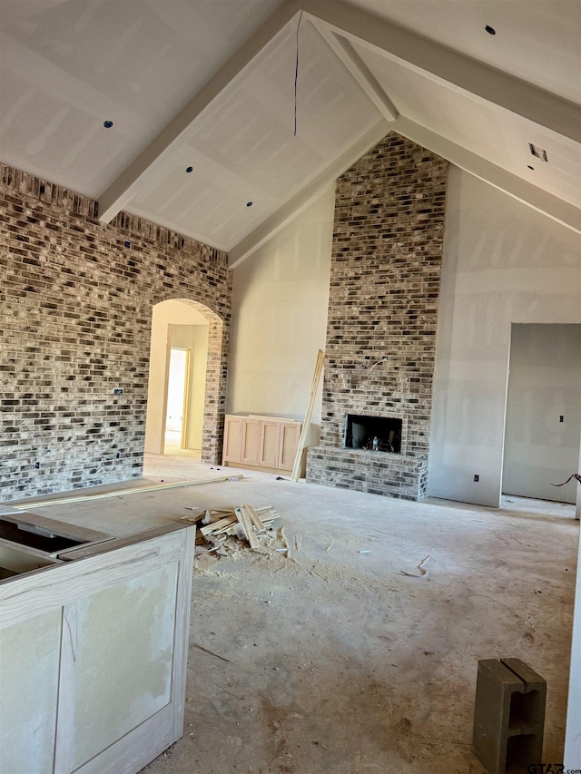 unfurnished living room featuring a large fireplace, beam ceiling, and high vaulted ceiling