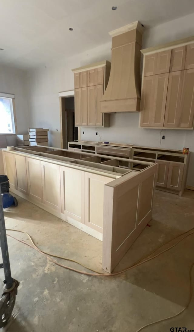 kitchen with light brown cabinetry and custom range hood