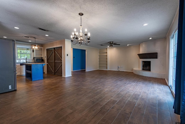 unfurnished living room featuring a barn door, dark hardwood / wood-style floors, a textured ceiling, and a large fireplace