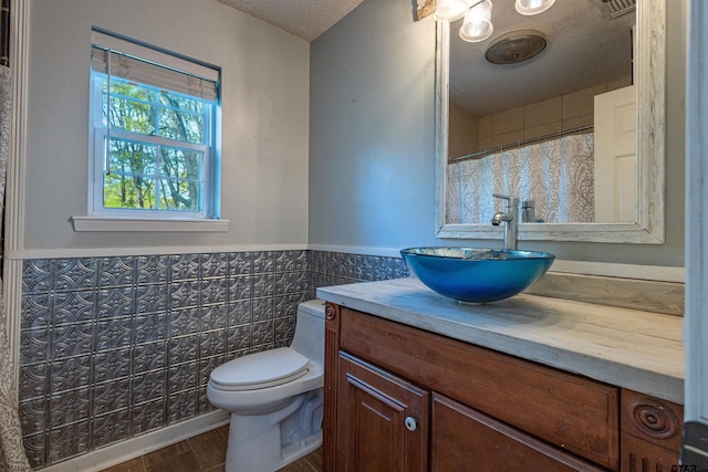 bathroom with a textured ceiling, wood-type flooring, vanity, toilet, and tile walls