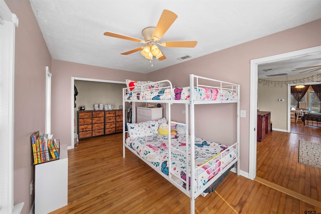 bedroom featuring a ceiling fan, wood-type flooring, visible vents, and baseboards